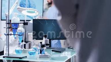 穿着白大褂的科学家使用一台数码平板电脑，然后在他的办公桌前放置